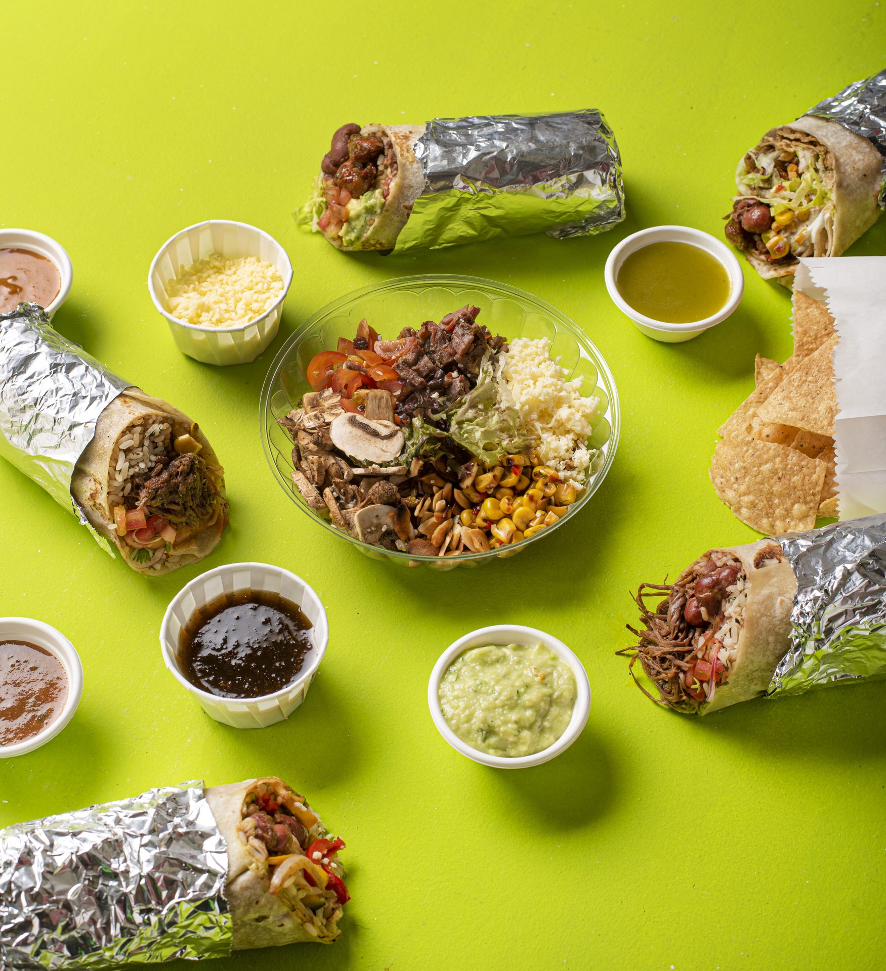 Mesa llena de burros y salsas sobre fondo verde lima